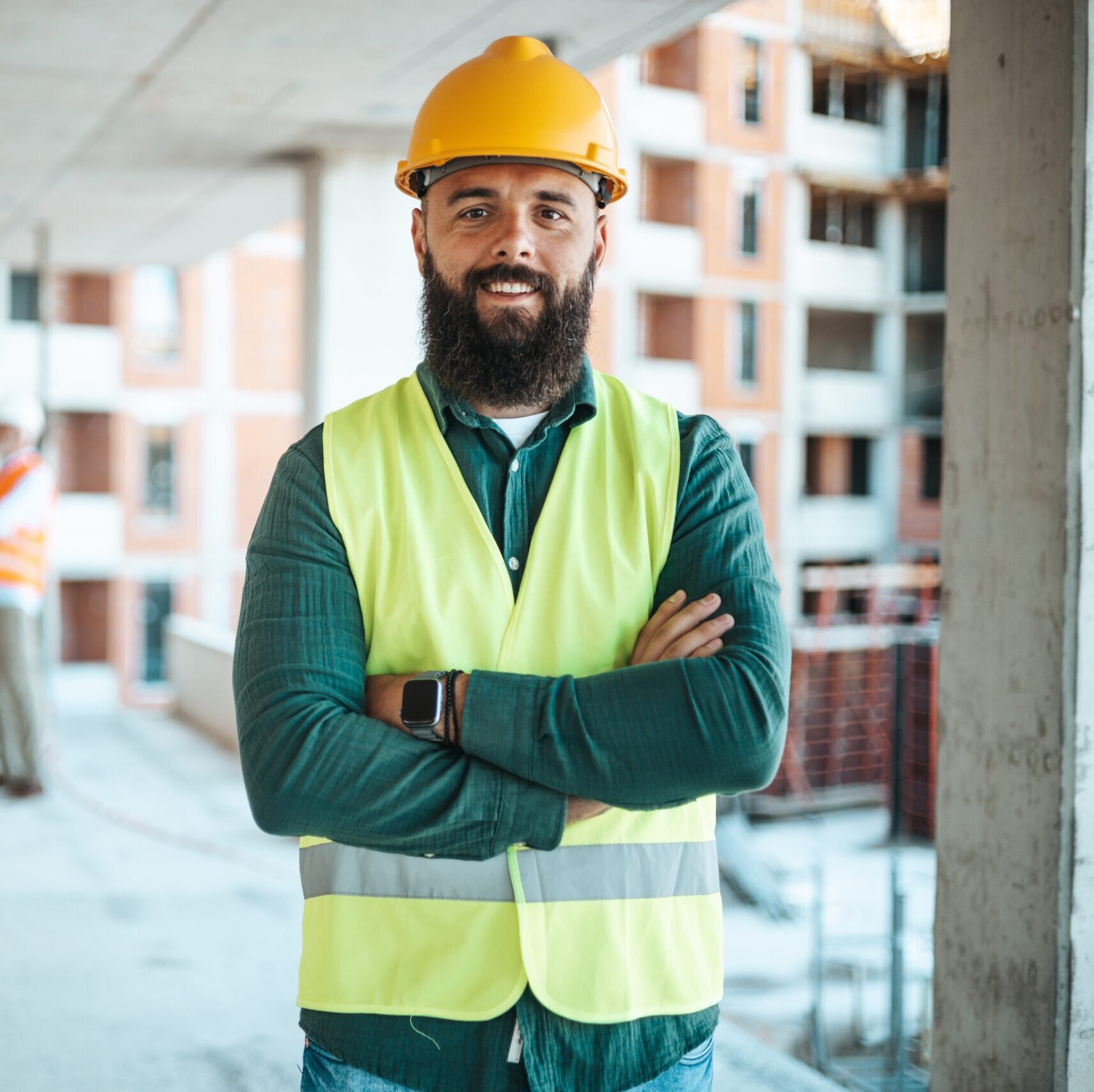 Man on construction site with arms crossed, smiling wearing a hardhat